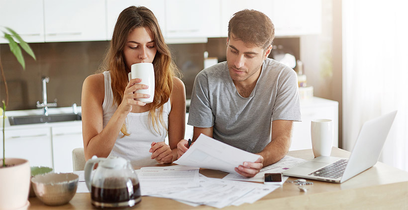 A man and a woman drinking coffee and looking over a pile of papers
