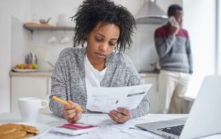 Woman looking at a gas bill and holding a pencil with a man in the background