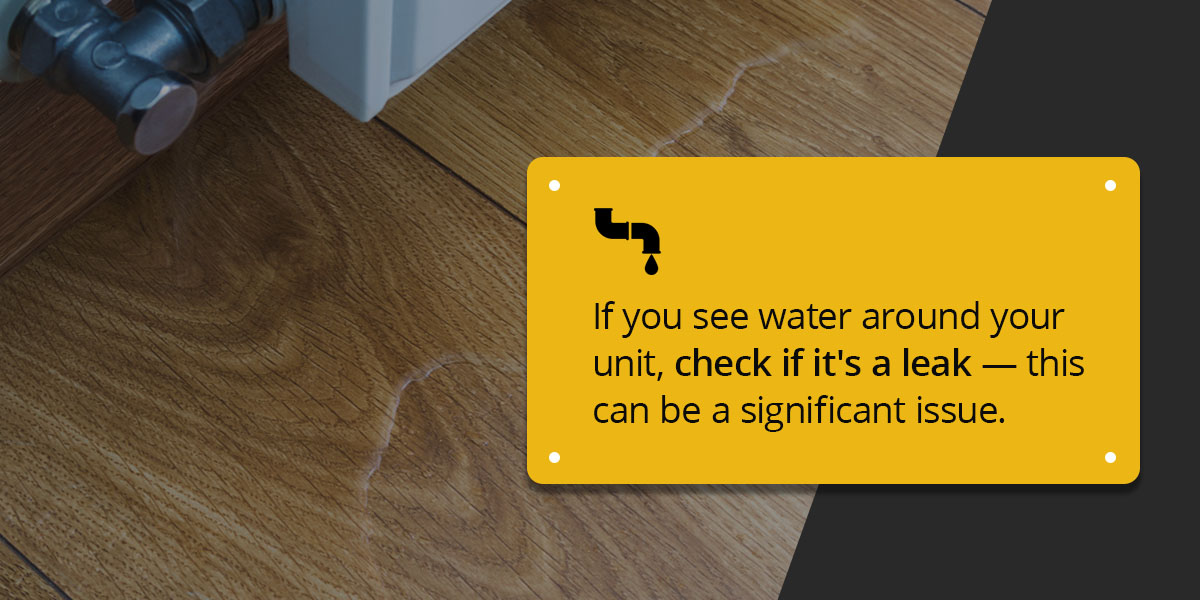 Water stains on wooden floor next to white baseboard with warning about checking for leaks