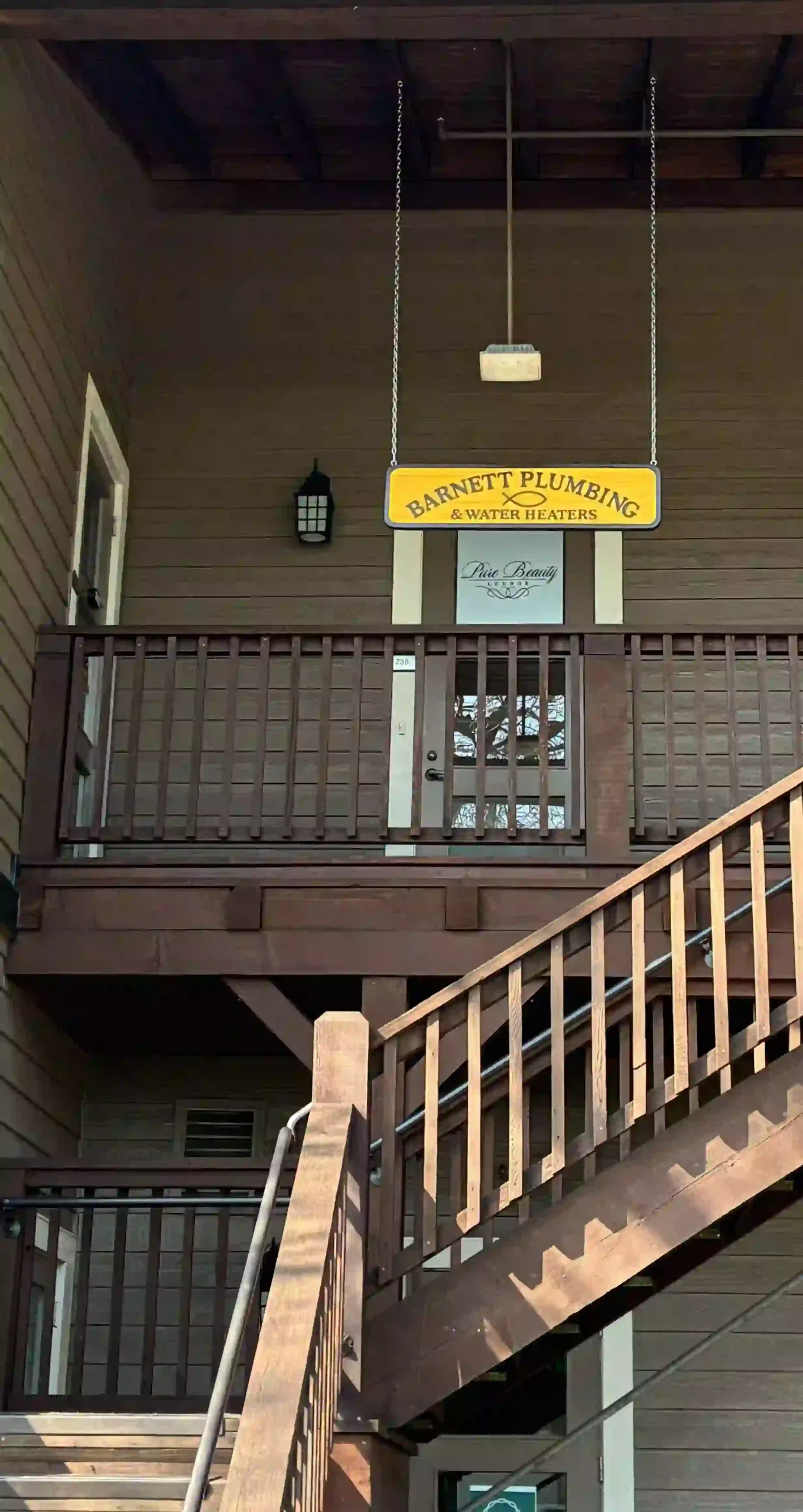 Barnett Plumbing & Water Heaters yellow hanging sign on storefront entrance with wooden railing.