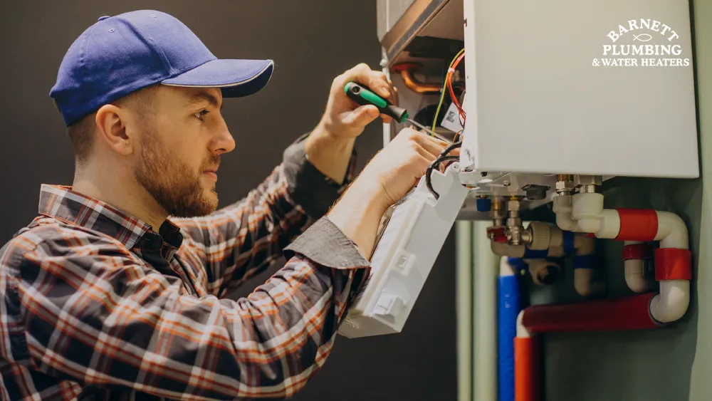 Plumber in blue cap working on water heater electrical connections with screwdriver