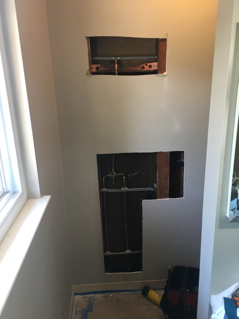 Wall cutouts reveal copper pipes for plumbing repiping, showing essential infrastructure work in progress.