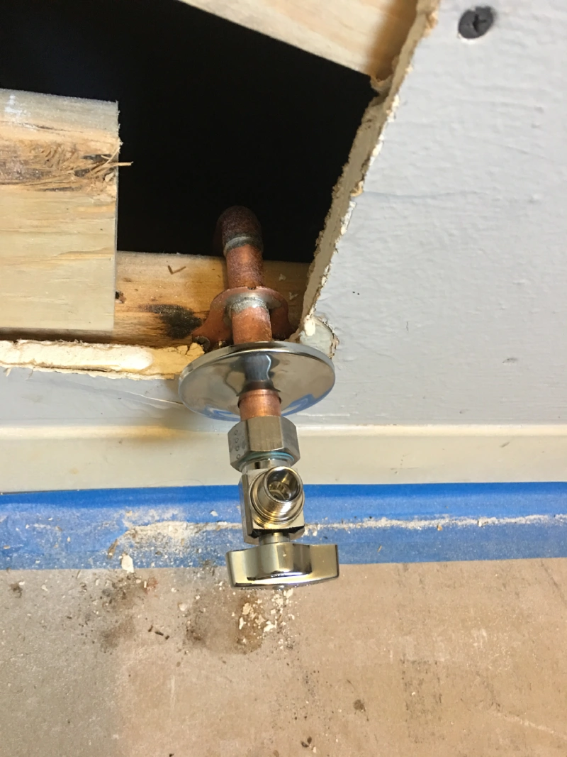 A new plumbing valve is installed in a wall cutout, showcasing repiping work with exposed copper pipes and a shiny fixture.