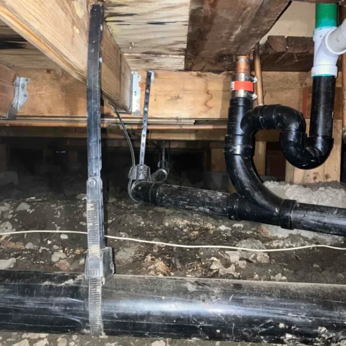 Under-floor view showing new plumbing pipes installed for repiping, secured to wooden beams, amid dirt and debris.