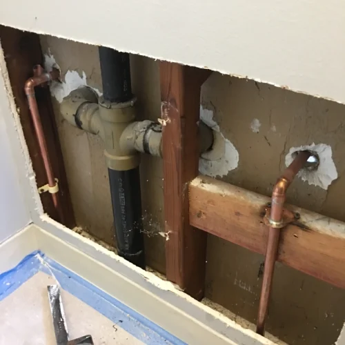Exposed wall shows plumbing work with new copper pipes, highlighting a repiping project in progress.