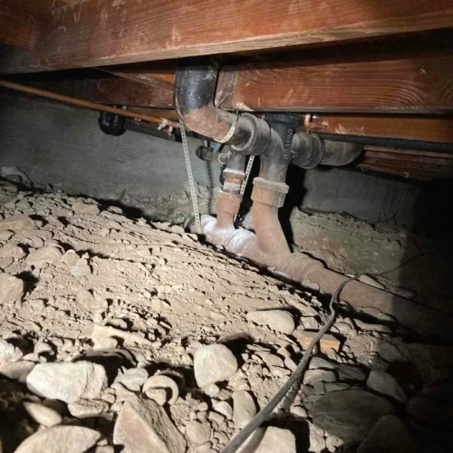 Crawl space with exposed pipes needing sewer repair, highlighting essential sewer services for maintenance and safety.