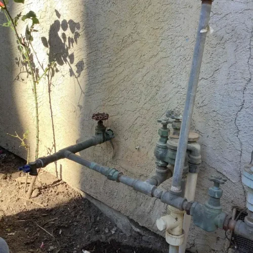 Pipes and valves against a wall indicate ongoing water line repair, with tools and soil nearby, hinting at recent work.