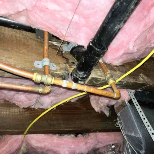 Copper pipes and insulation in a basement ceiling show a recent water line repair, with pink insulation surrounding them.